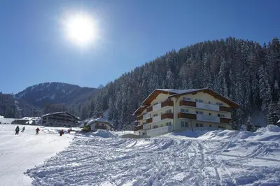 a building on a snow covered mountain with people in front at Garni Hotel Bel Vert in Selva di Val Gardena