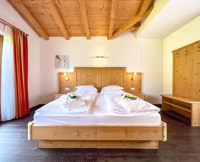 a bedroom with a large bed with white sheets at Garni Hotel Bel Vert in Selva di Val Gardena