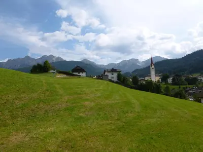 a green hill with a town and a church on it at Posterhof in Valdaora