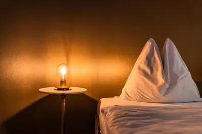 a small table with a lamp next to a bed at goldfinger + suites in Lana