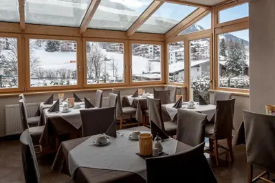 a dining room with tables and chairs and windows at Hotel Garni Villa Park in Ortisei