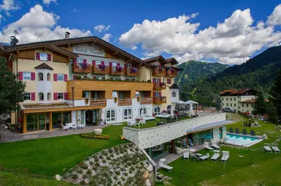 a large building with a pool in front of it at Nature Wellness Hotel Renato in Vigo di Fassa