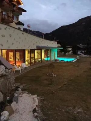 a building with a swimming pool next to a house at Nature Wellness Hotel Renato in Vigo di Fassa