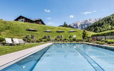 a swimming pool with umbrellas and chairs and a house at Hotel Portillo Dolomites 1966' in Selva di Val Gardena