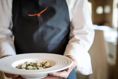 a person holding a white plate with food on it at Adler Spa Resort Dolomiti in Ortisei