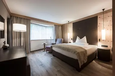 a hotel room with a large bed and a chair at Adler Spa Resort Dolomiti in Ortisei
