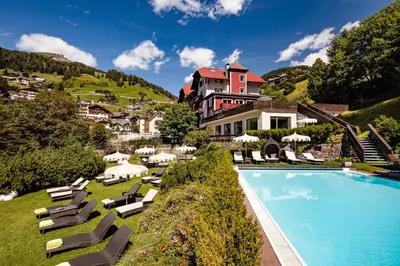 a resort with a swimming pool and chairs and a building at Grand Hotel Wolkenstein in Selva di Val Gardena
