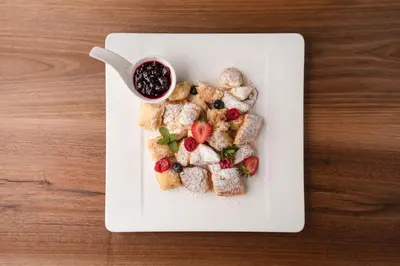 a white plate with food on a wooden table at Hotel Girlanerhof in Appiano sulla Strada del Vino