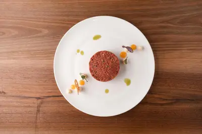 a white plate with a burger on a wooden table at Hotel Girlanerhof in Appiano sulla Strada del Vino