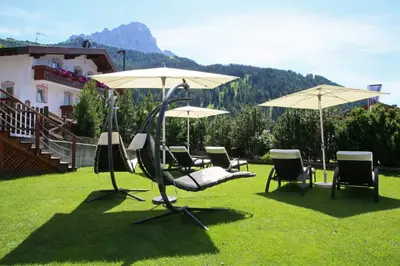 a group of chairs and umbrellas in the grass at Hotel Condor in Selva di Val Gardena