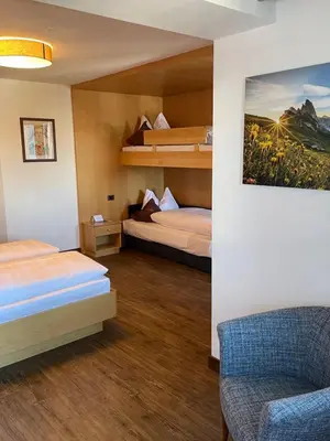 a hotel room with two beds and a chair at Hotel Condor in Selva di Val Gardena