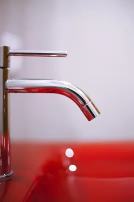 a chrome bathroom faucet on a red sink at Hotel Ariston in Bolzano