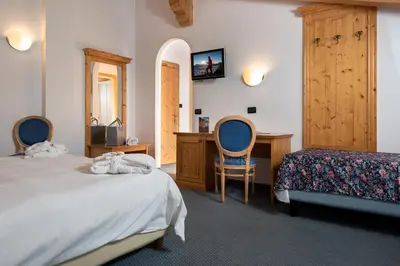 a bedroom with two beds and a desk at Hotel Valacia in Pozza di Fassa