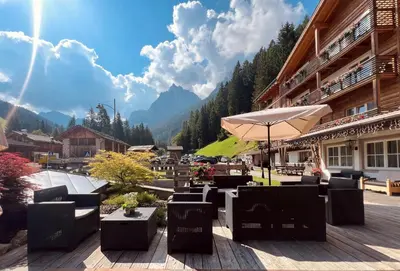 a patio with tables and chairs and an umbrella at Hotel Valacia in Pozza di Fassa