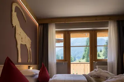a bedroom with a bed and a large window at Hotel Somont in Selva di Val Gardena