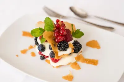 a white plate with a dessert with berries and whipped cream at Hotel Kiendl in Schenna