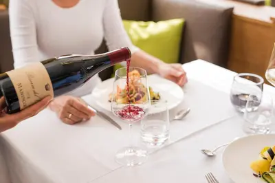 a woman pouring wine into a wine glass at Hotel Kiendl in Schenna