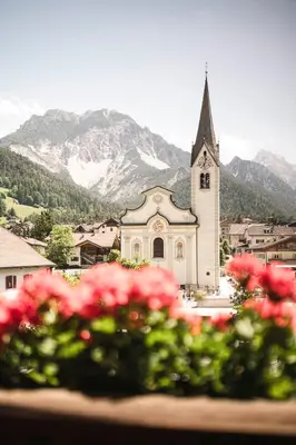 a church with a steeple and a bunch of pink flowers at Christophorus Mountain Residence in San Vigilio Di Marebbe