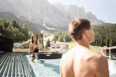 a man and a woman sitting in a swimming pool at Hotel Plan de Gralba - das Berghotel in Selva di Val Gardena