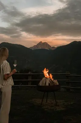 a woman standing next to a fire pit with a glass of wine at Herol - my mountain retreat in Luson
