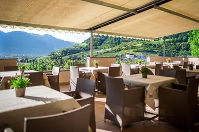 a restaurant with tables and chairs with mountains in the background at Pension An Der Linde in Lagundo
