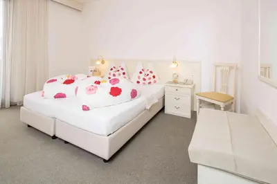 a white bedroom with two beds and a chair at Pension An Der Linde in Lagundo