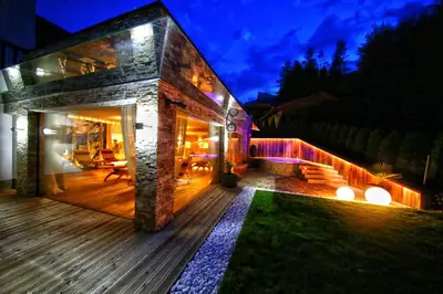 a house with a wooden deck at night at La Bercia Alpine Lodge & Spa in La Villa