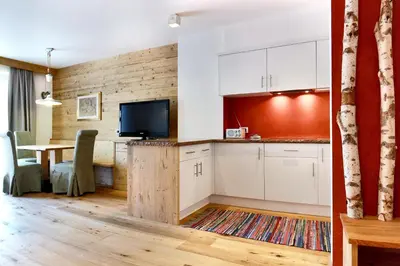 a kitchen with white cabinets and a table with a tv at La Bercia Alpine Lodge & Spa in La Villa