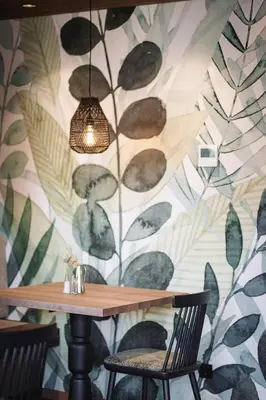 a table with two chairs and a wall with leaves at Hotel Garni Andrianerhof in Andrian