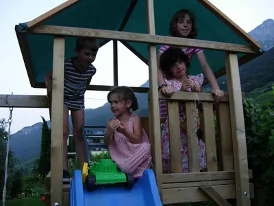 three children playing in a wooden play house at Residence Nesslerheim in Termeno
