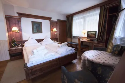 a bedroom with a bed with white sheets and a desk at Hotel Garni Concordia - Dolomites Home in Selva di Val Gardena