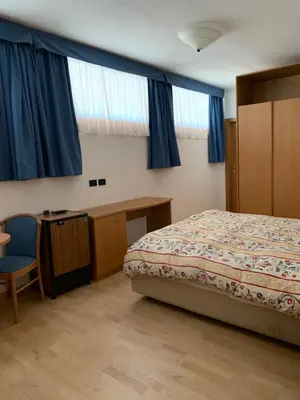 a bedroom with a bed and a desk and blue curtains at Garni Enrosadira in Vigo di Fassa