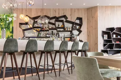 a dining room with a bar with green chairs at Hotel Rosengarten (Schenna Resort) in Schenna
