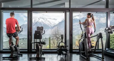 a man and woman exercising in a gym looking out the window at Hotel Rosengarten (Schenna Resort) in Schenna