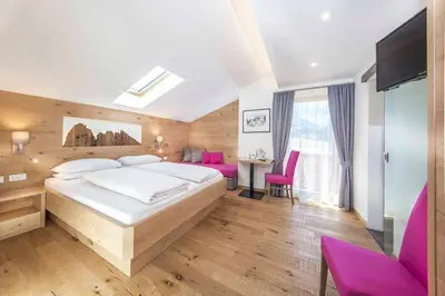 a bedroom with a large bed and pink chairs at Hotel Garni Morene in Selva di Val Gardena