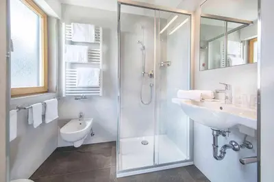 a white bathroom with a shower and a sink at Hotel Garni Morene in Selva di Val Gardena