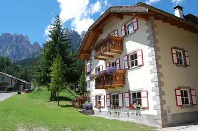 a white building with red windows and a balcony at Appartamenti Casari in Pozza di Fassa