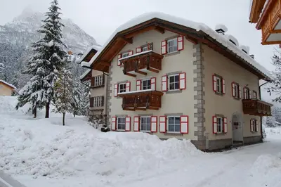 a building with snow on the ground in front of it at Appartamenti Casari in Pozza di Fassa