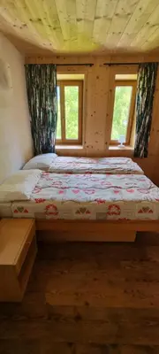 a bed in a room with two windows at Appartamenti Casari in Pozza di Fassa