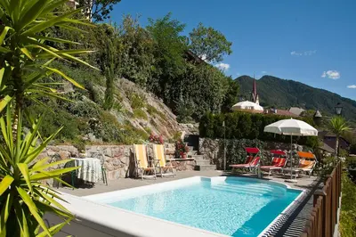 a swimming pool in a yard with chairs and an umbrella at Garni Pramstrahler in Chiusa