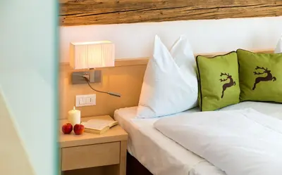 a bedroom with a bed with green and white pillows at Hotel Regglbergerhof in Nova Ponente