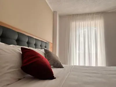 a bed with two red pillows and a window at Hotel Rododendro Val di Fassa in Campitello di Fassa