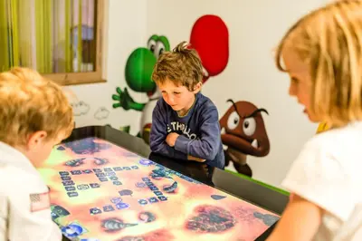 a young boy sitting at a table with two children at Romantik & Family Hotel Gardenia***S in Selva di Val Gardena
