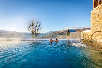 two people swimming in a pool with a fountain at Tratterhof Mountain Sky Hotel in Maranza