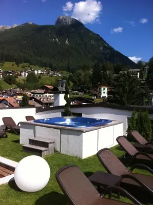 a patio with chairs and a pool and a mountain at Sport Hotel S. Vigilio in Moena
