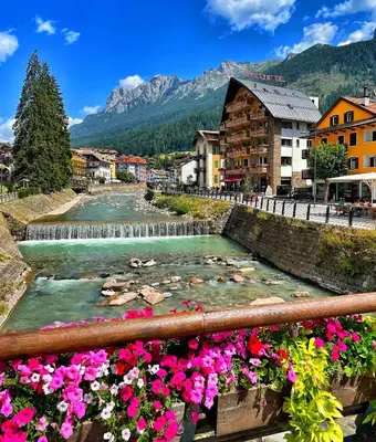 a river in a town with flowers and a waterfall at Sport Hotel S. Vigilio in Moena