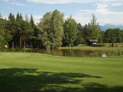 a golf course with a pond and trees in the background at Hotel Roen Ruffrè-Mendola in Mendola