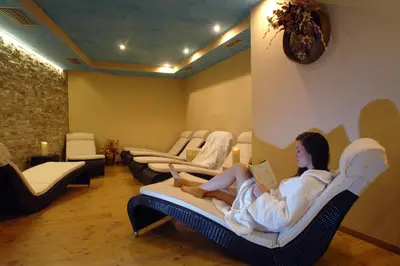 a woman sitting in a chair reading a book at Cimon Dolomites Hotel in Predazzo