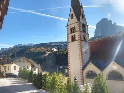 a church with a tower with a mountain in the background at Villa Ula Verda- Apartments Marianna in Santa Cristina in Val Gardena
