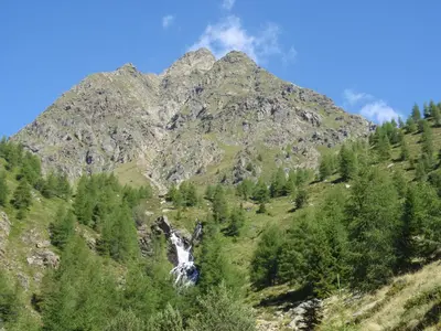 a mountain with a waterfall in front of it at Hotel Blitzburg in Brunico